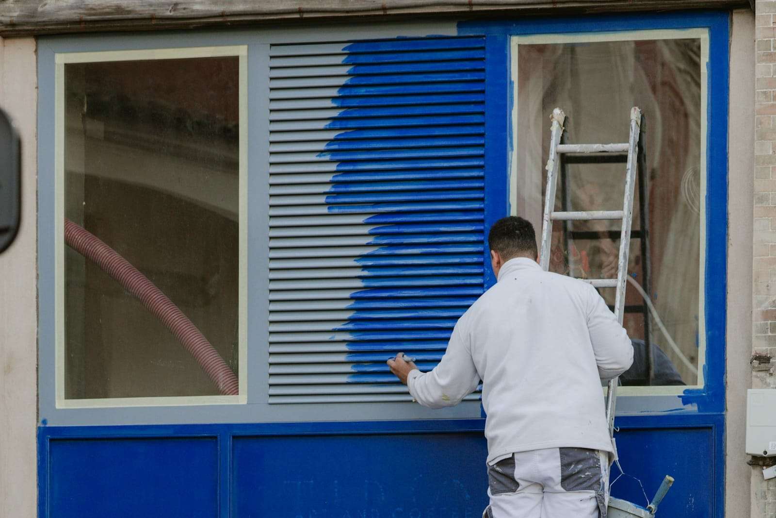 Painter on a ladder rolling blue paint onto an exterior window shutter