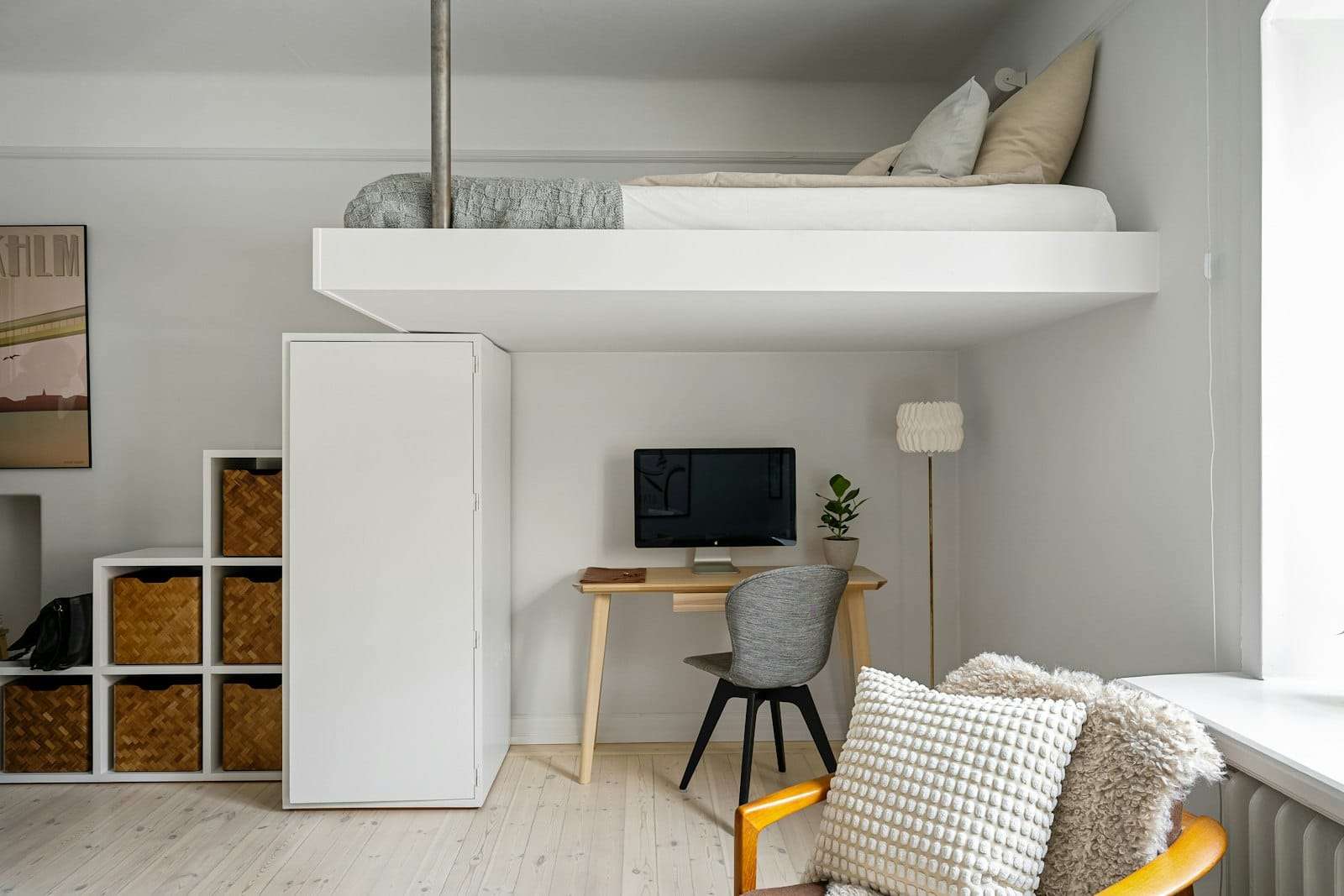 Small white bedroom with a loft bed over a desk and light timber floors