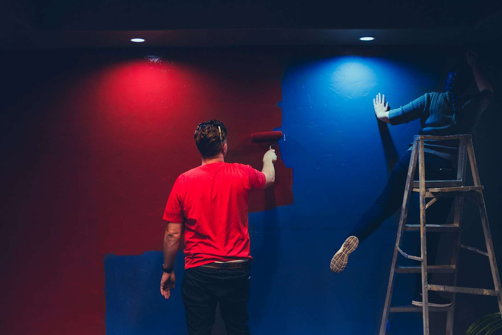 Two people painting a room red and blue, one with a roller and one on a stepladder