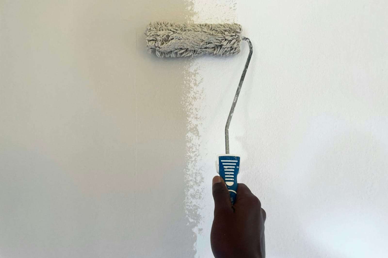 Hand rolling a first stripe of white paint onto a wall