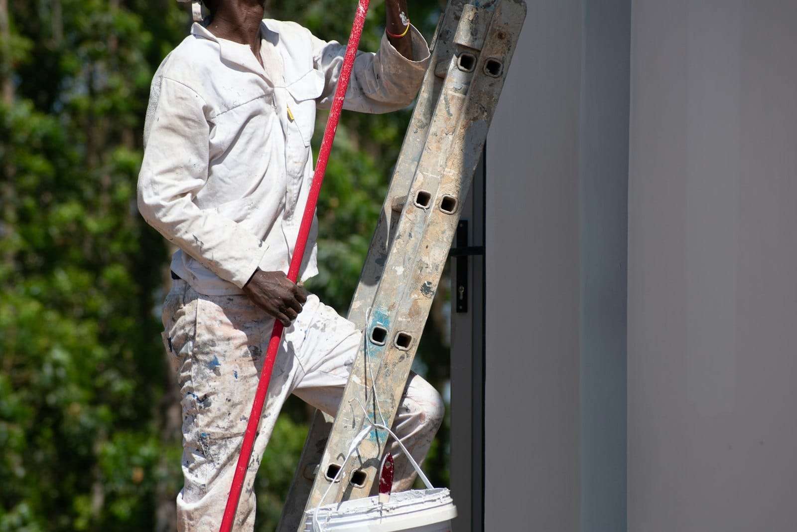 Painter in white overalls on a ladder with a roller and paint bucket