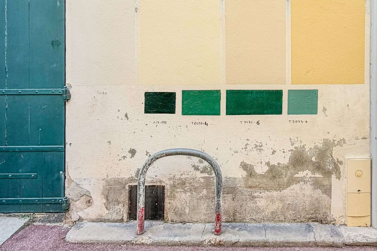 Rows of cream and green paint test patches on a weathered wall