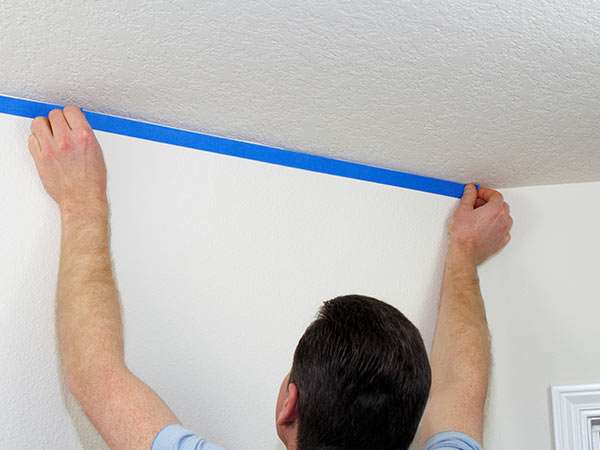 Painter applying masking tape along a ceiling line