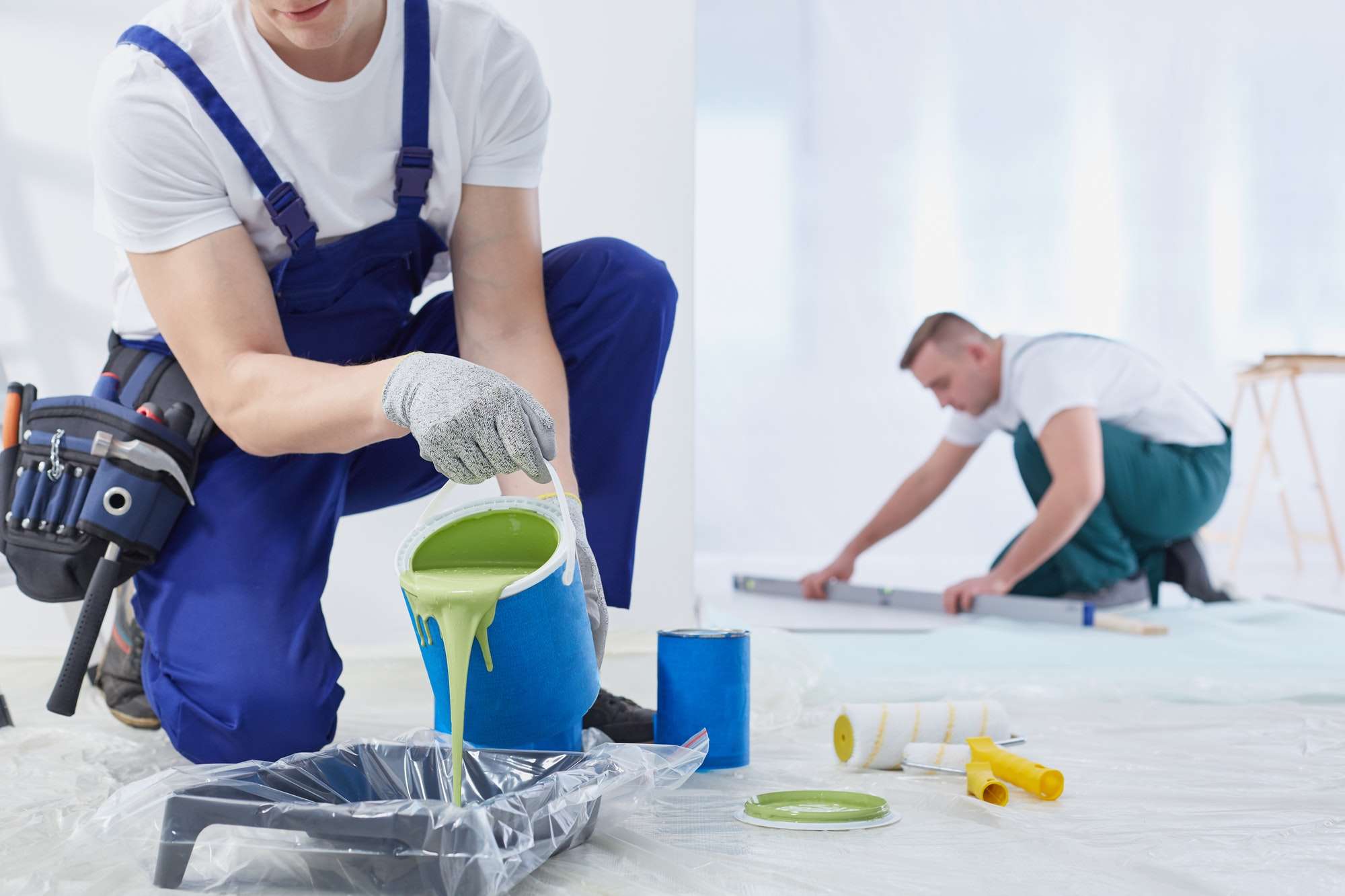 Two painters preparing paint and painting a wall